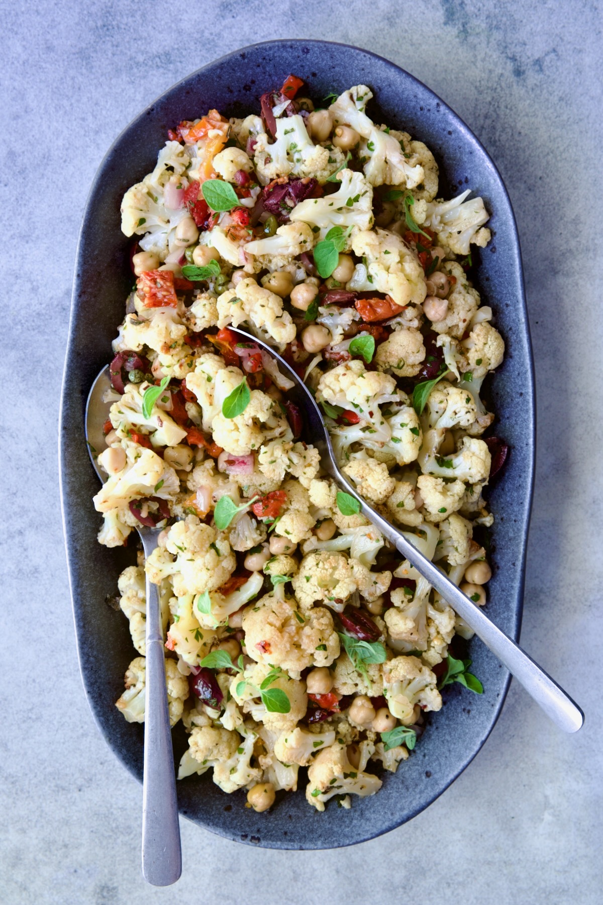 Roasted Cauliflower Salad on gray speckled platter with serving utensils.