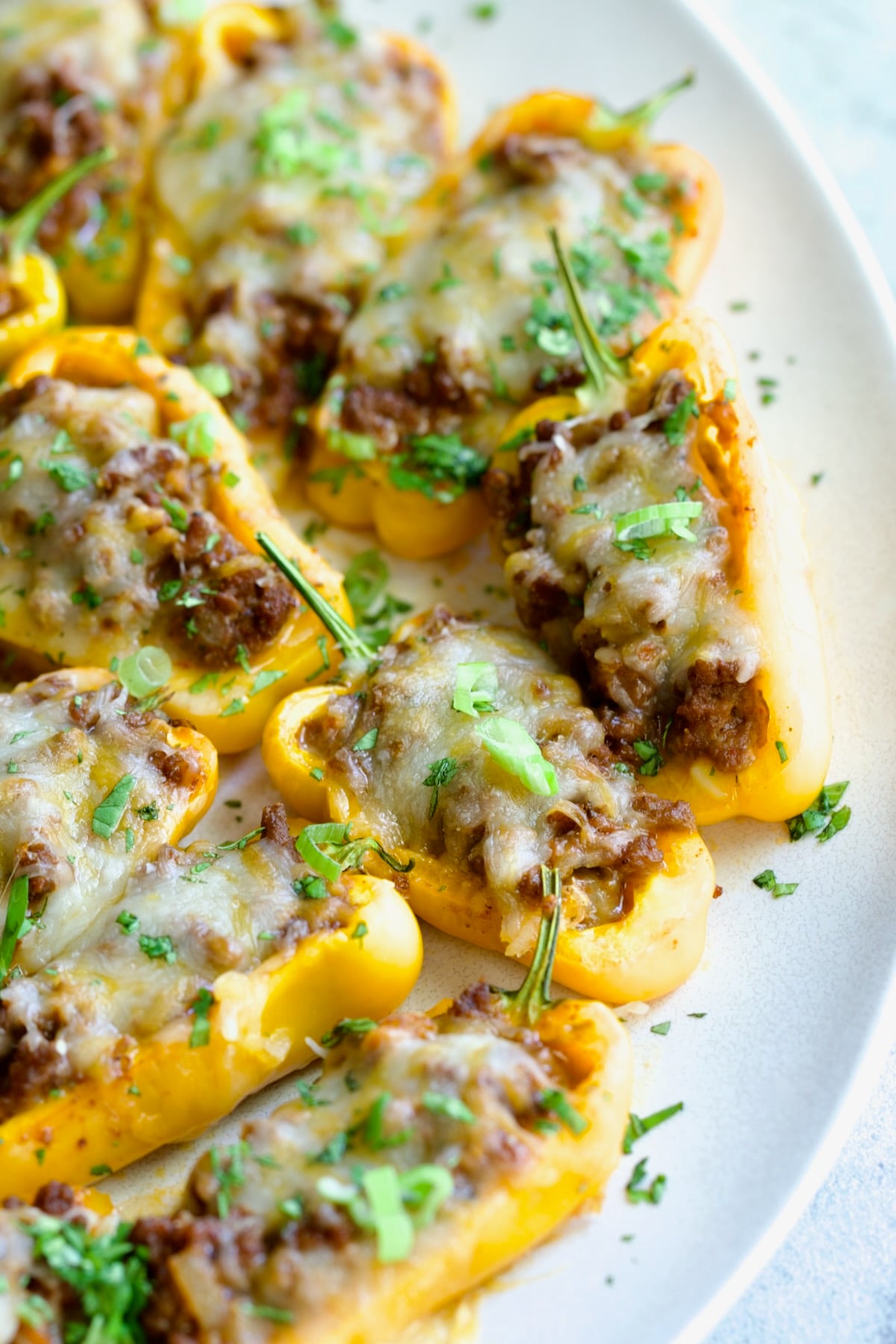 Close-up of Taco-Stuffed Mini Peppers on white oval platter garnished with thinly sliced scallion and chopped cilantro.
