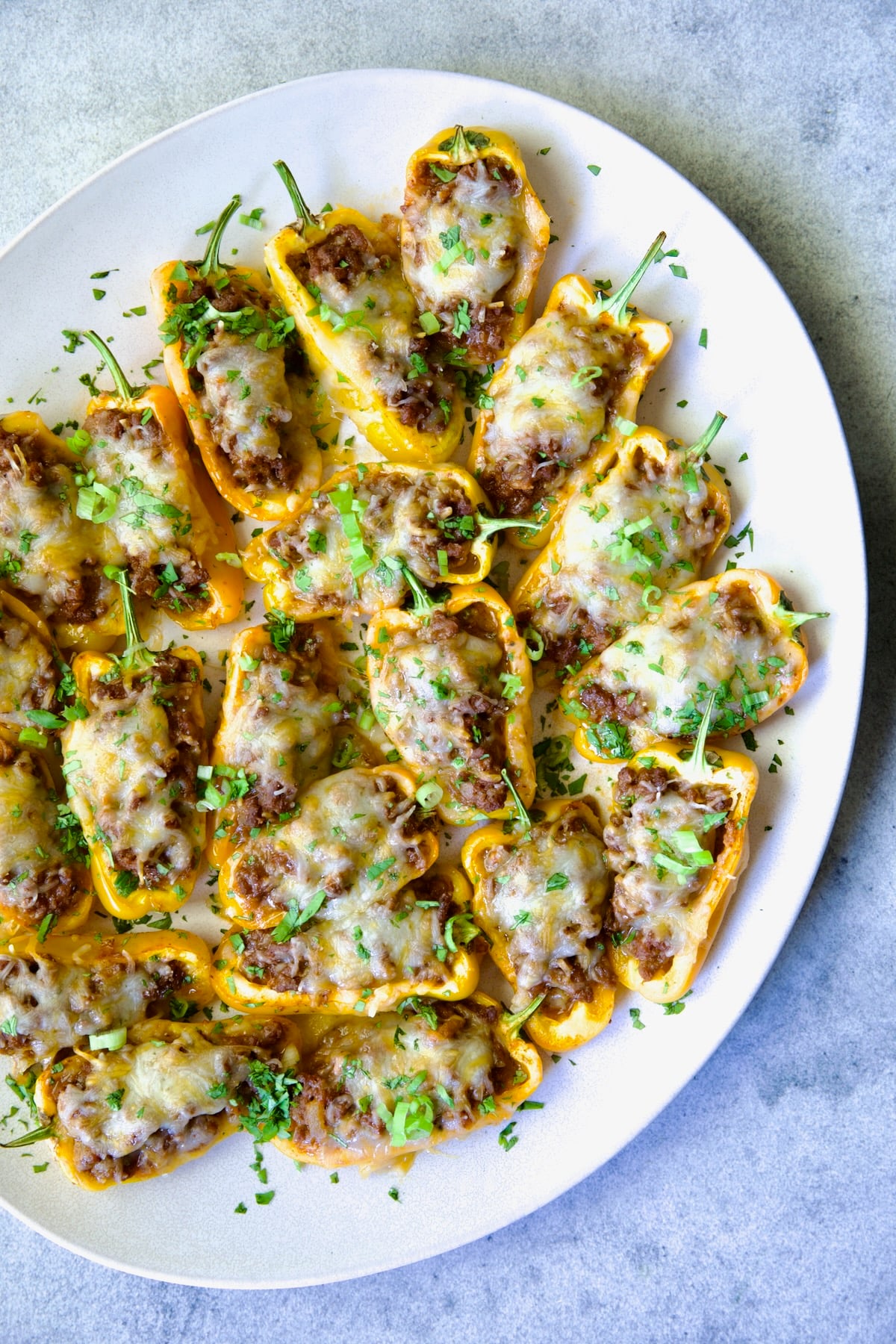 Taco-Stuffed Mini Peppers on white oval platter garnished with thinly sliced scallion and chopped cilantro.
