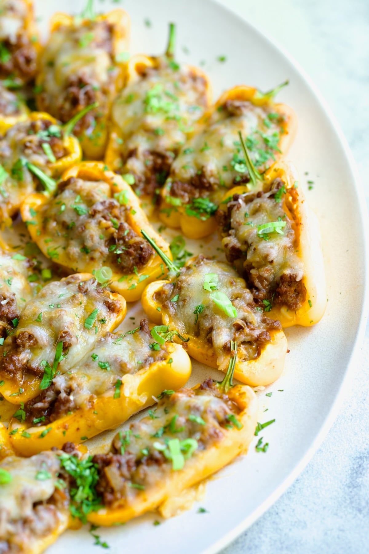 Close-up of Taco-Stuffed Mini Peppers on white oval platter garnished with thinly sliced scallion and chopped cilantro.