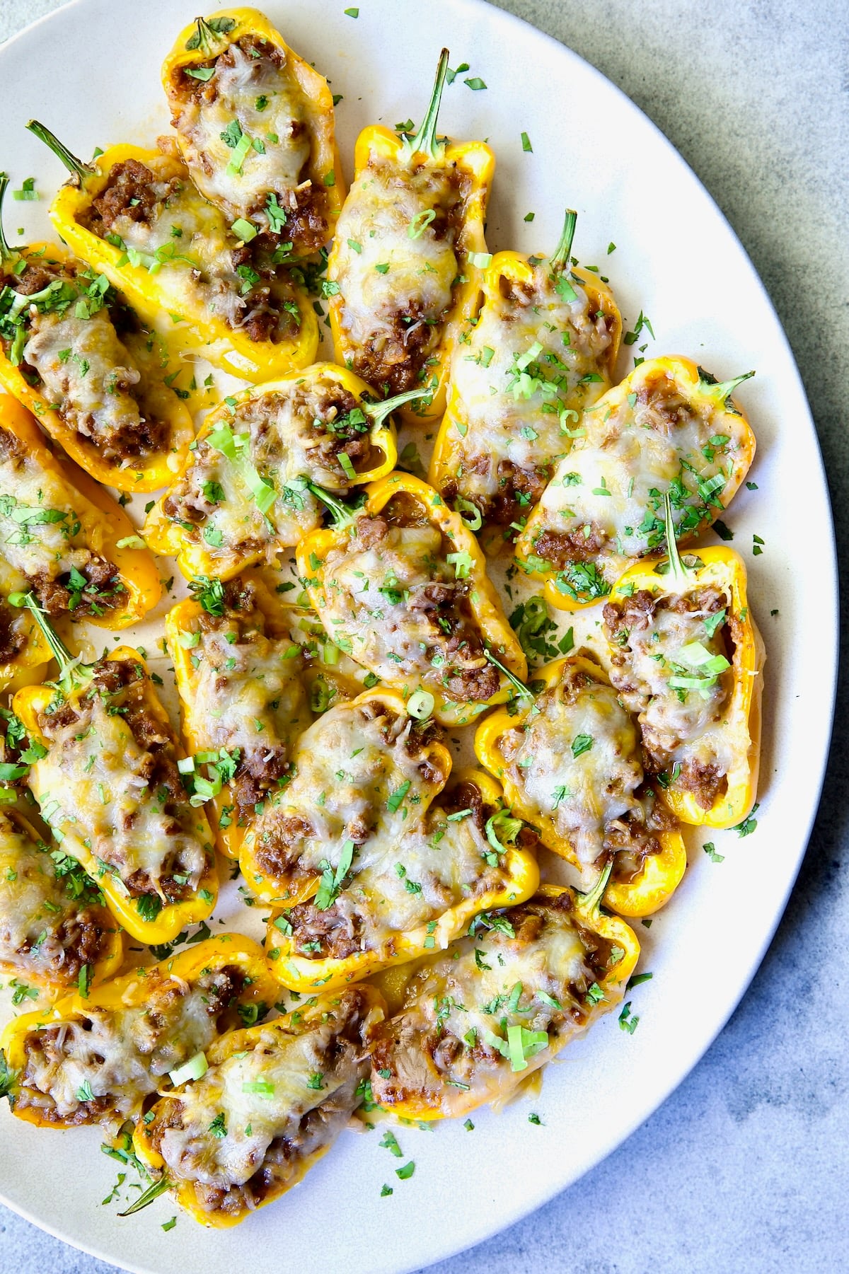 Taco-Stuffed Mini Peppers on white oval platter garnished with thinly sliced scallion and chopped cilantro.