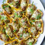 Taco-Stuffed Mini Peppers on white oval platter garnished with thinly sliced scallion and chopped cilantro.