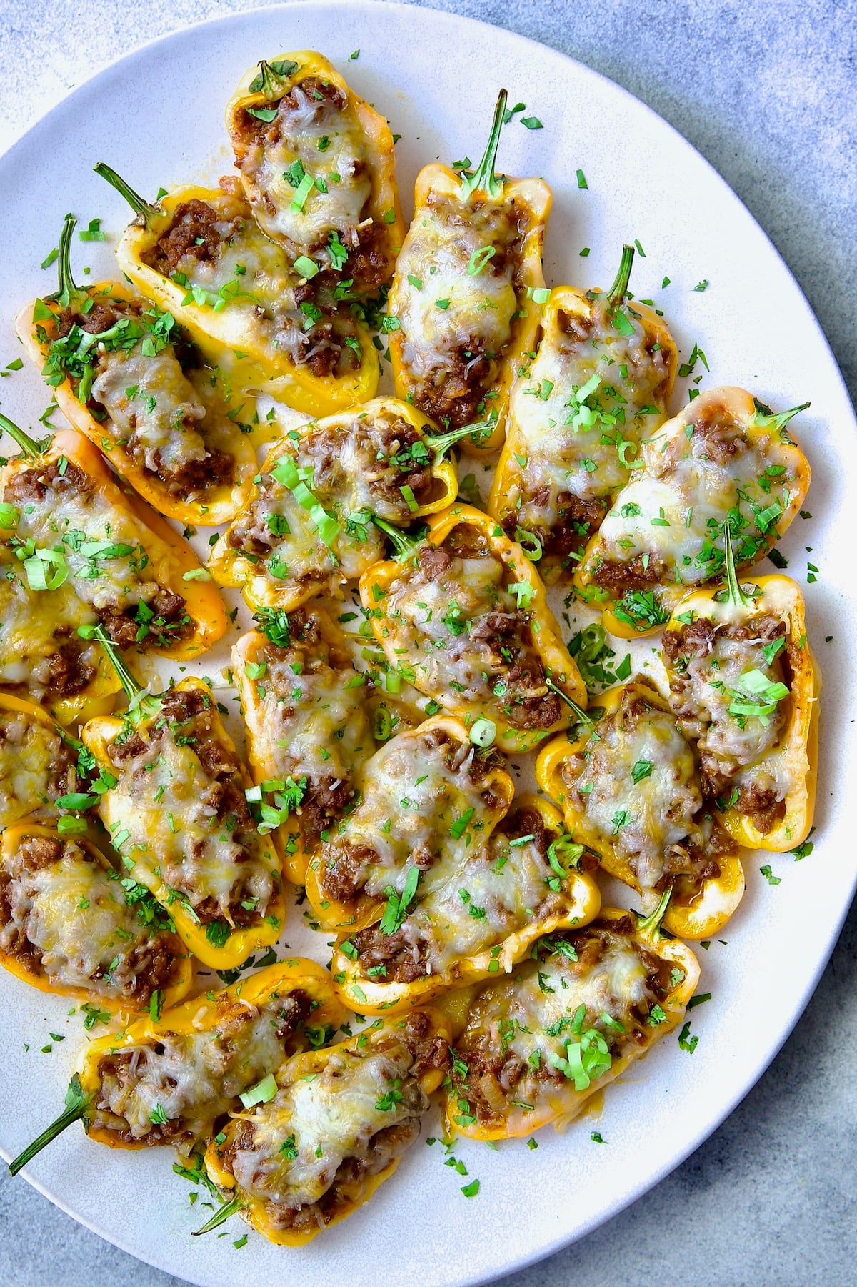 Taco-Stuffed Mini Peppers on white oval platter garnished with thinly sliced scallion and chopped cilantro.
