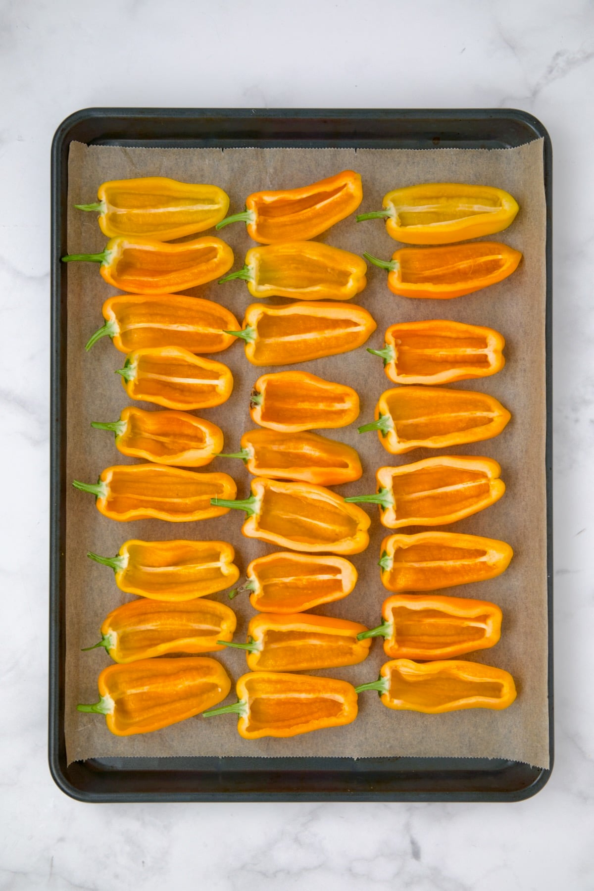 Halved yellow mini peppers on parchment paper lined baking sheet.
