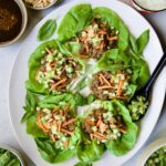 Vietnamese Beef Lettuce Wraps on oval white platter with lime wedges and accompaniments around it.