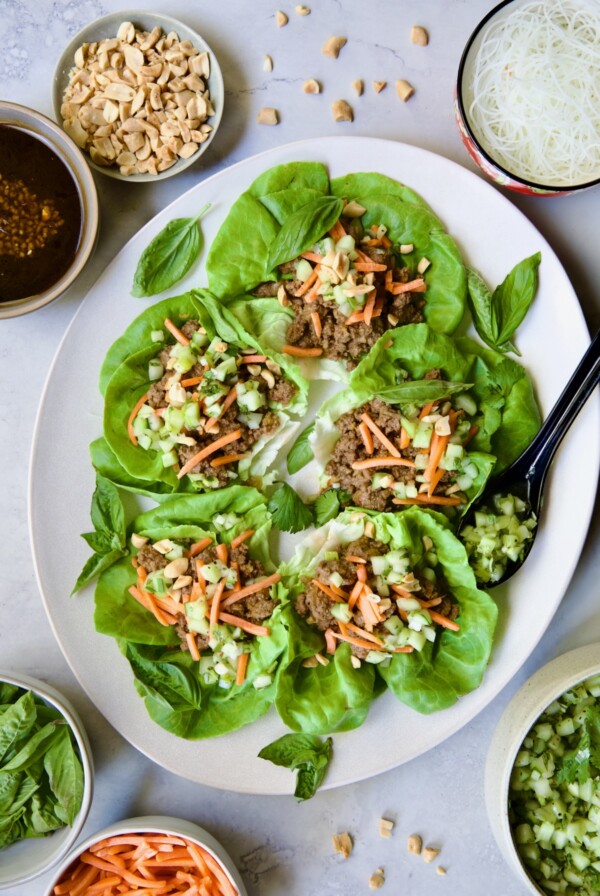 Vietnamese Beef Lettuce Wraps on oval white platter with lime wedges and accompaniments around it.