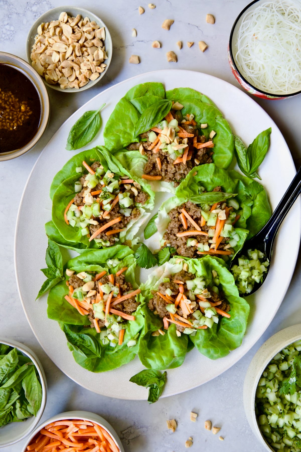 Vietnamese Beef Lettuce Wraps on oval white platter with lime wedges and accompaniments around it.