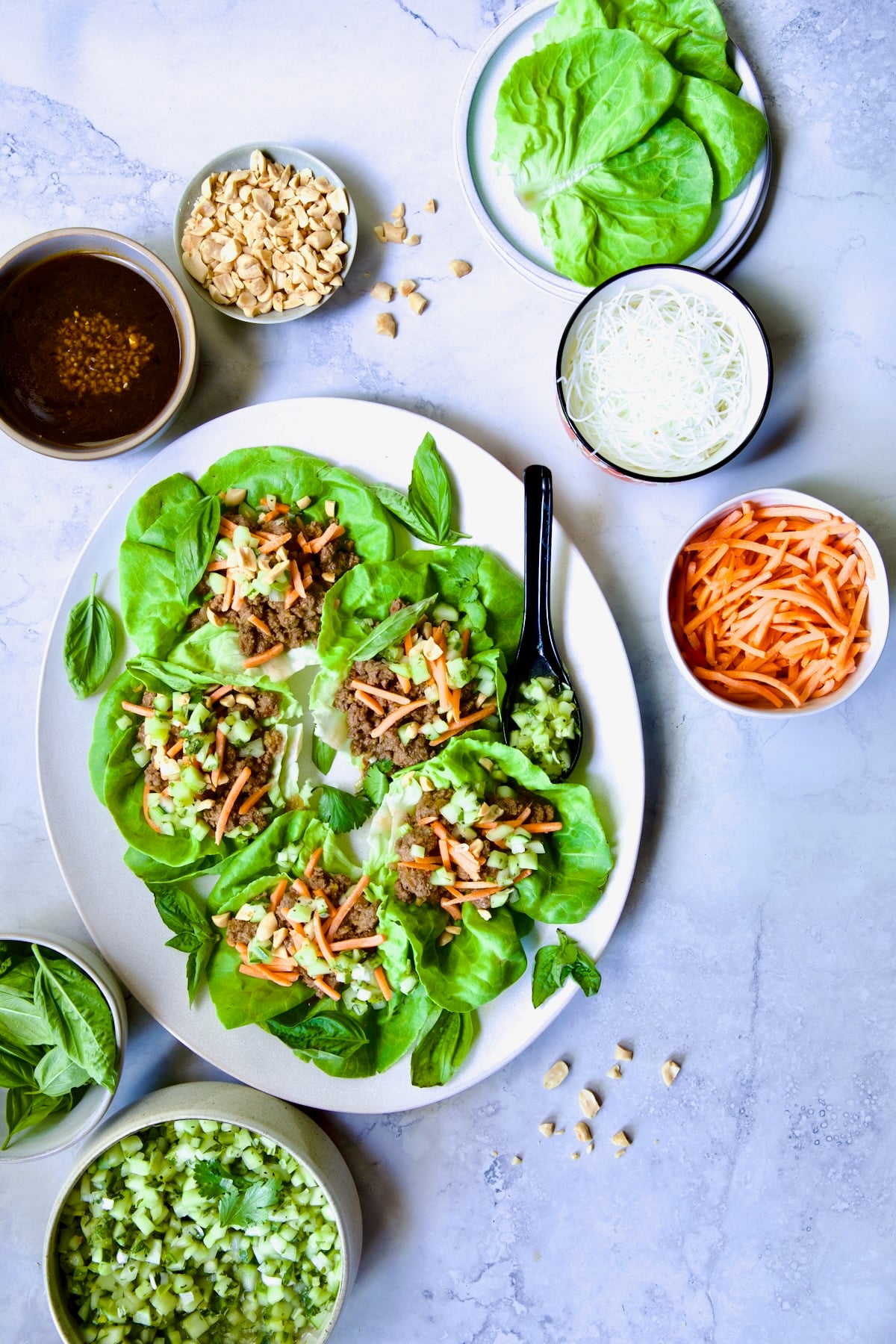Vietnamese Beef Lettuce Wraps on oval white platter with lime wedges and accompaniments around it.