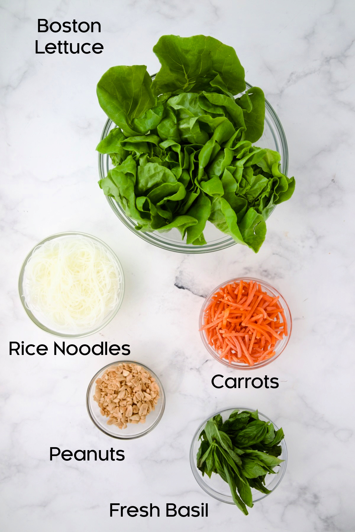 Lettuce, rice noodles, carrots, peanuts and fresh basil in glass bowls.