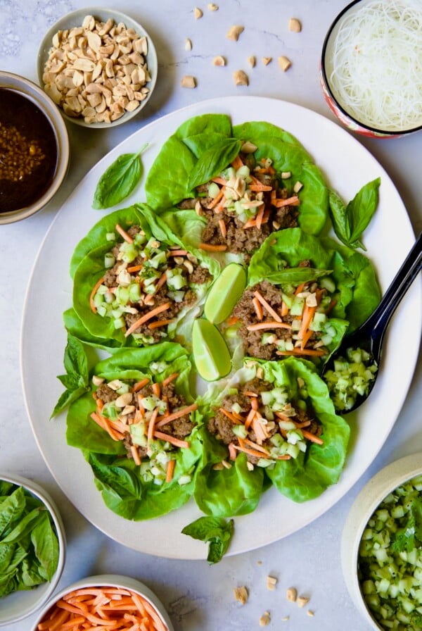 Vietnamese Beef Lettuce Wraps on oval white platter with lime wedges and accompaniments around it.