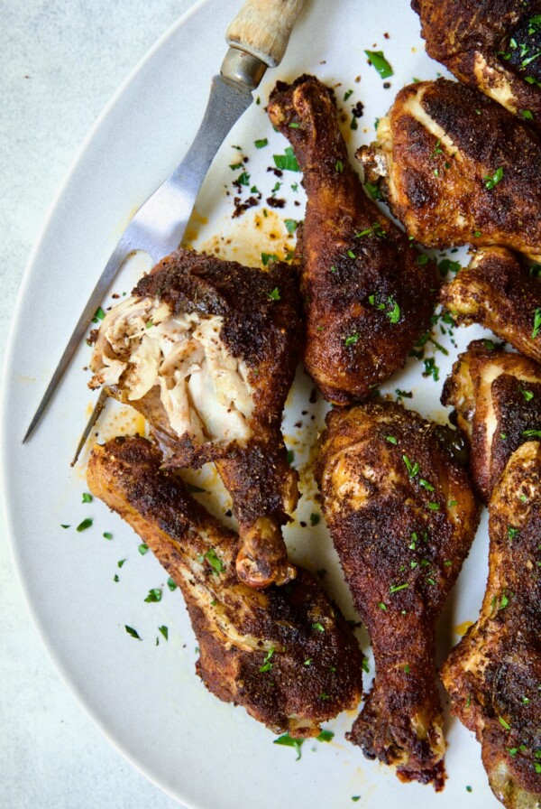Baked Cajun Chicken Drumsticks on oval white platter with one semi-shredded.