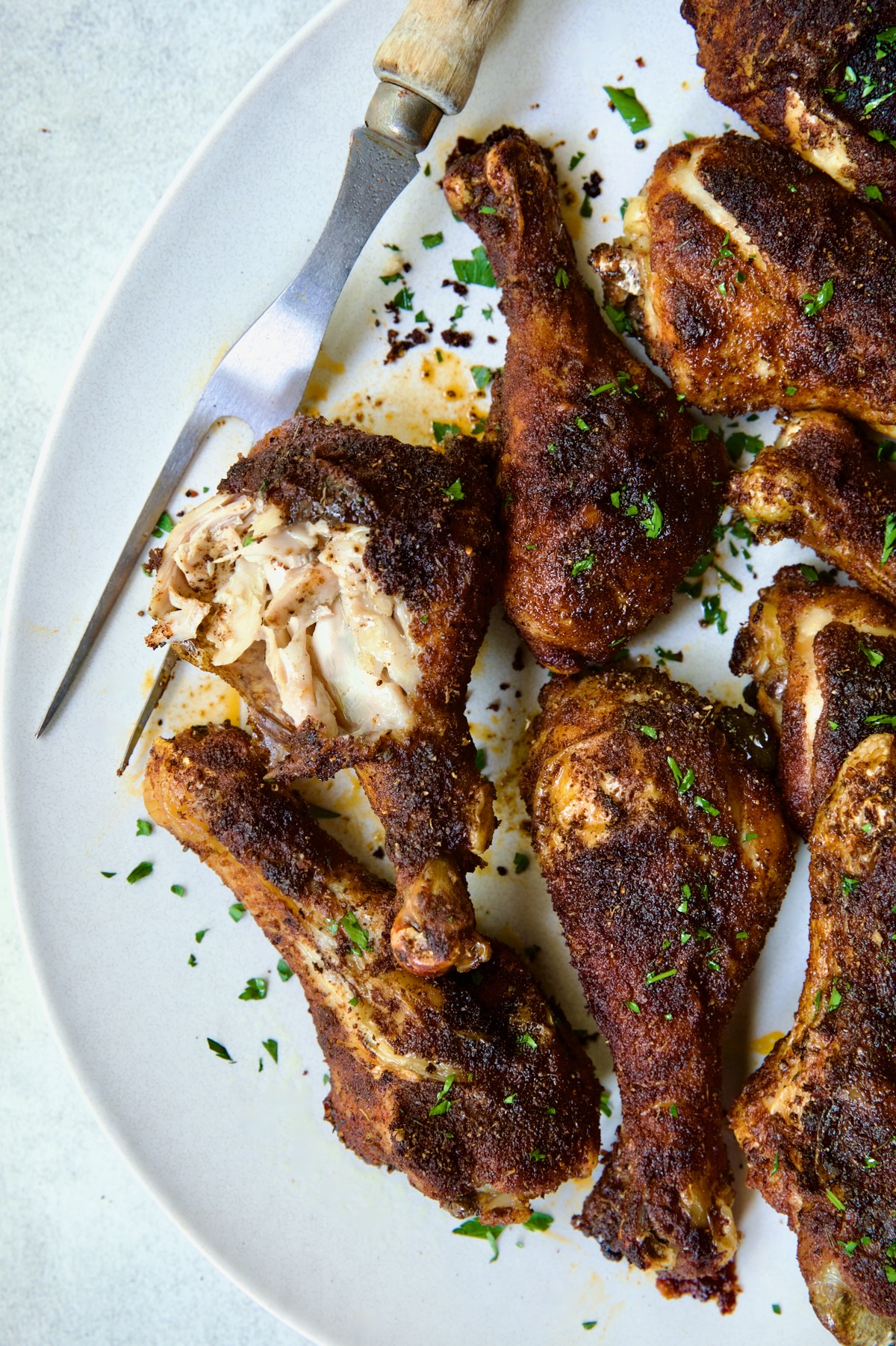 Baked Cajun Chicken Drumsticks on oval white platter with one semi-shredded.