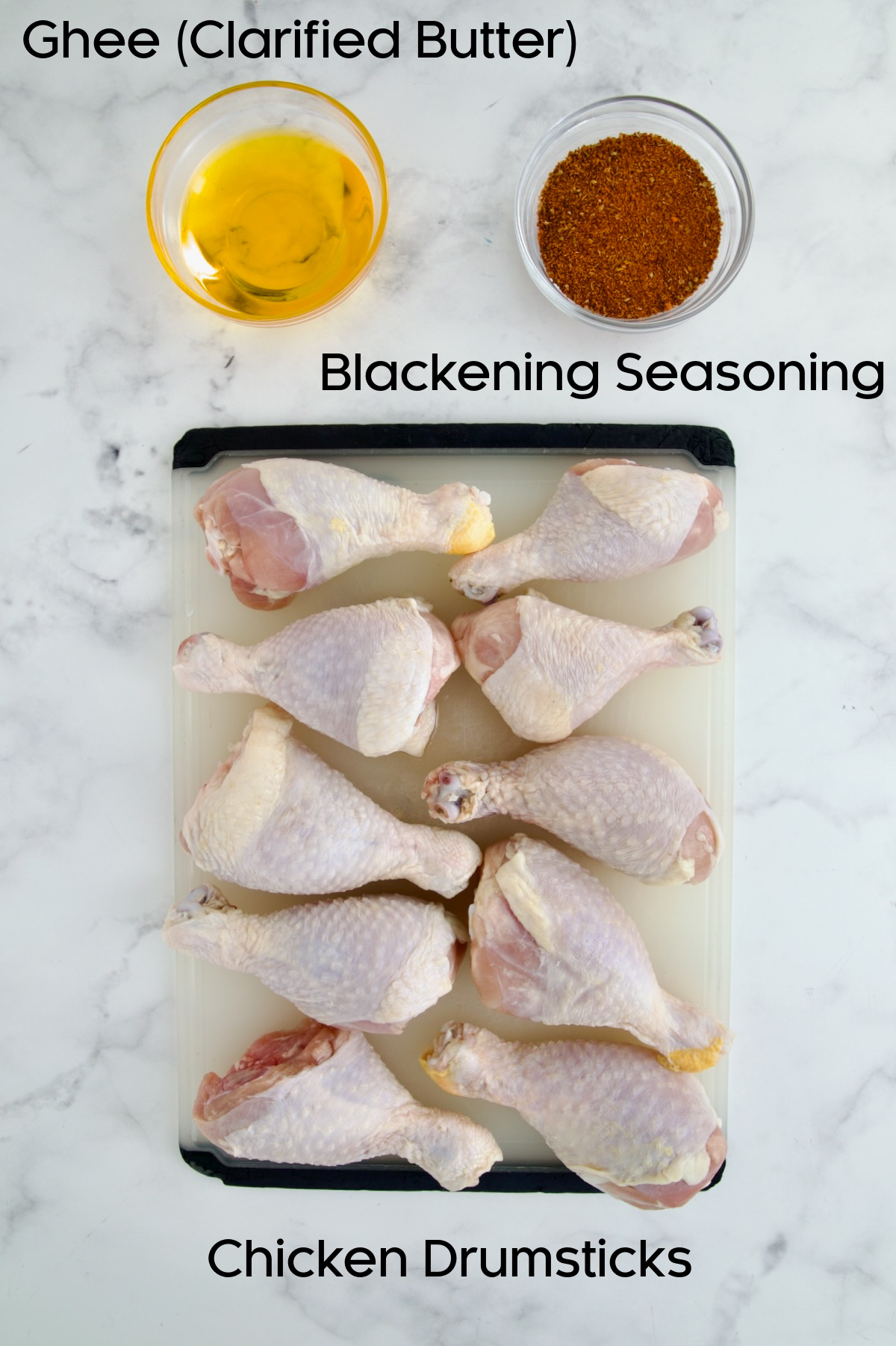 Ten uncooked chicken drumsticks, clarified butter in a bowl and blackening seasoning in a bowl.