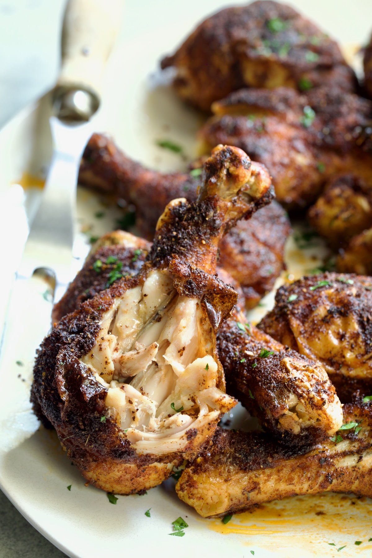 Baked Cajun Chicken Drumsticks on oval white platter with one semi-shredded.