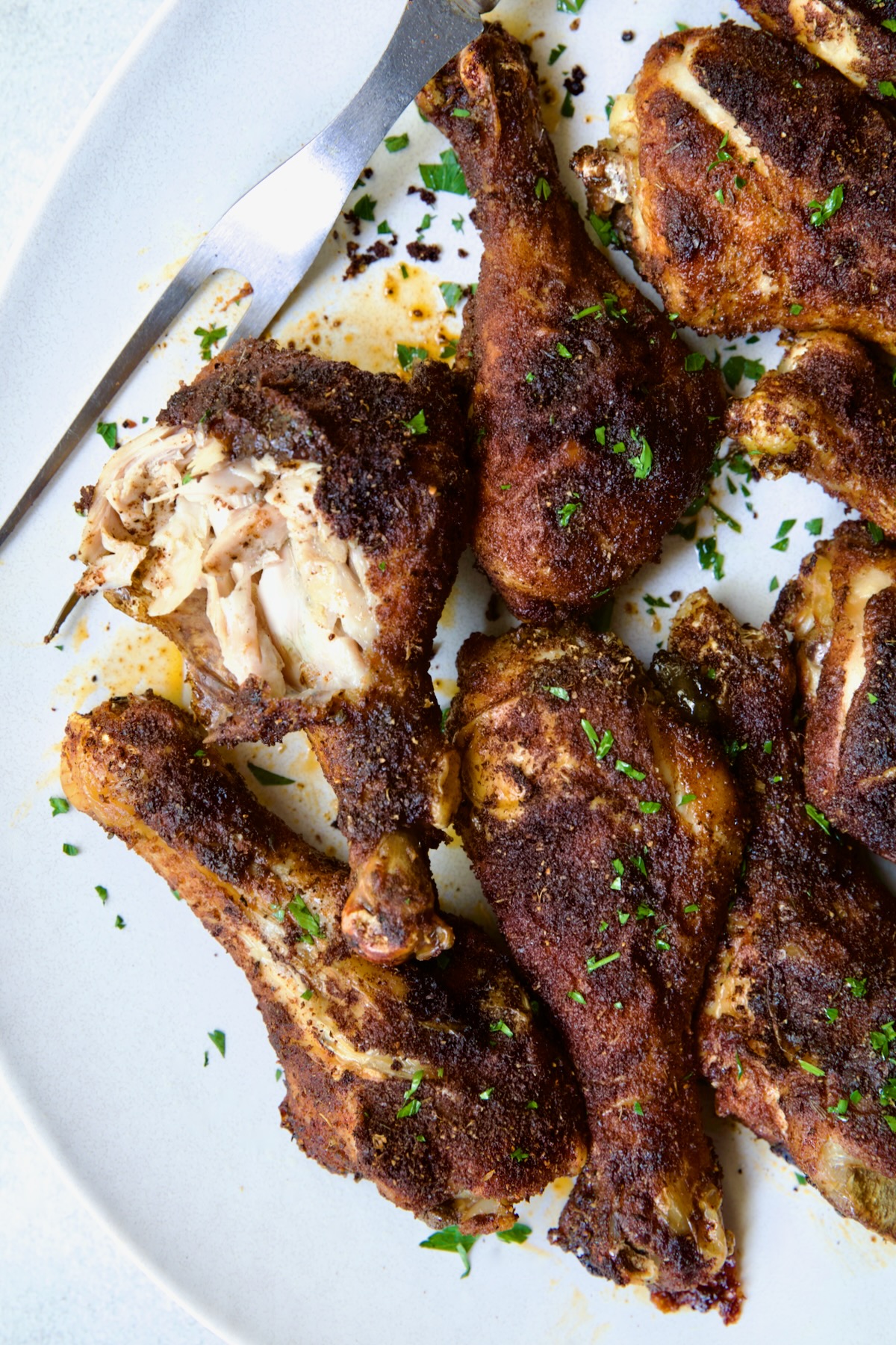 Baked Cajun Chicken Drumsticks on oval white platter with one semi-shredded.