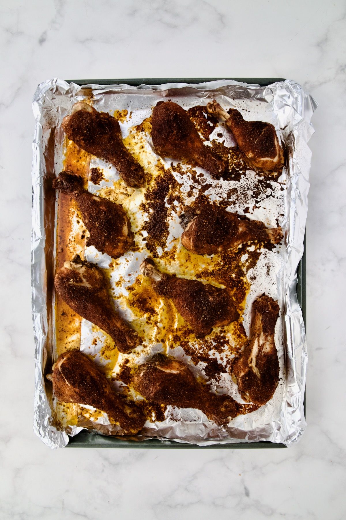 Ten cooked Baked Cajun Chicken Drumsticks on aluminum foil-lined rimmed sheet pan.