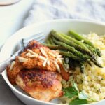 Chicken with Romesco in white dinner bowl with asparagus and cauliflower rice.
