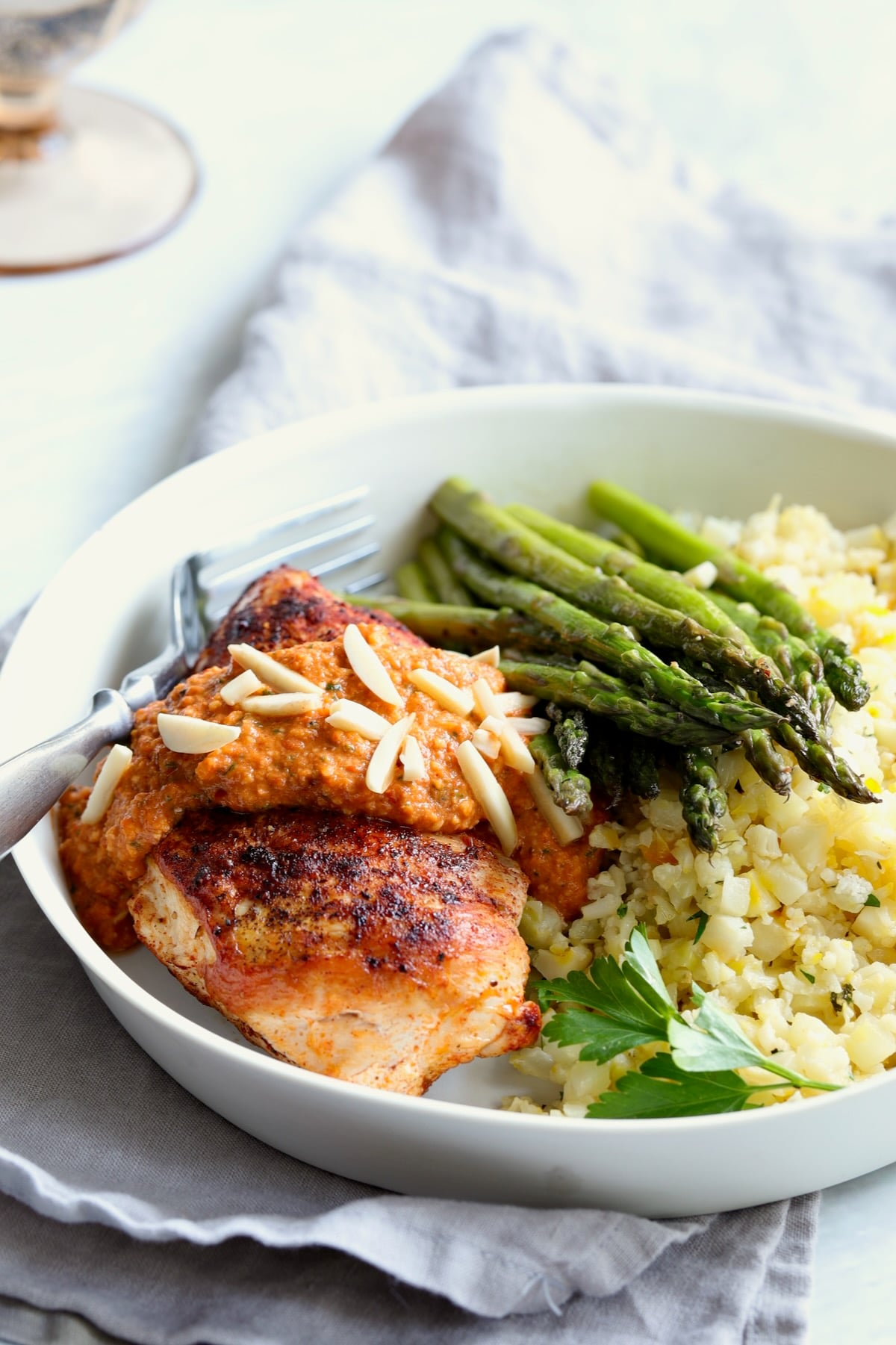 Chicken with Romesco in white dinner bowl with asparagus and cauliflower rice.