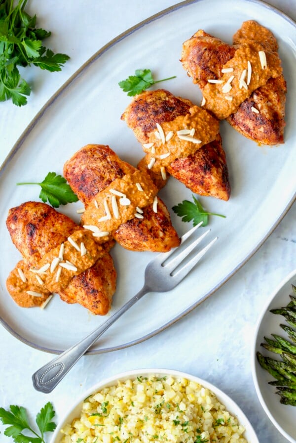 Four servings of Chicken with Romesco on gray-rimmed platter with serving fork.