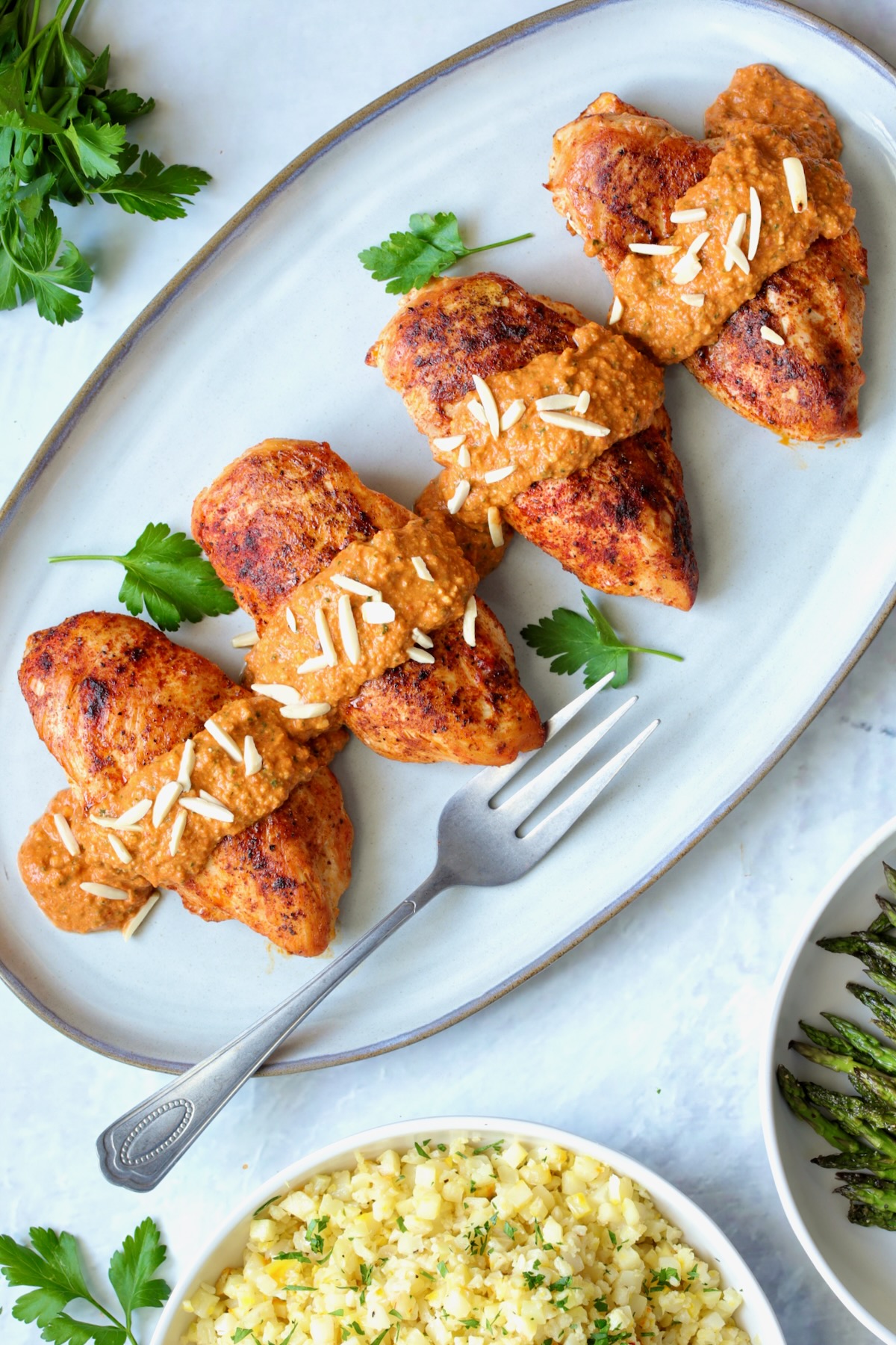 Four servings of Chicken with Romesco on gray-rimmed platter with serving fork.