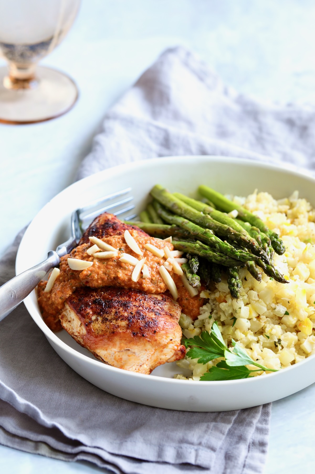 Chicken with Romesco in white dinner bowl with asparagus and cauliflower rice.