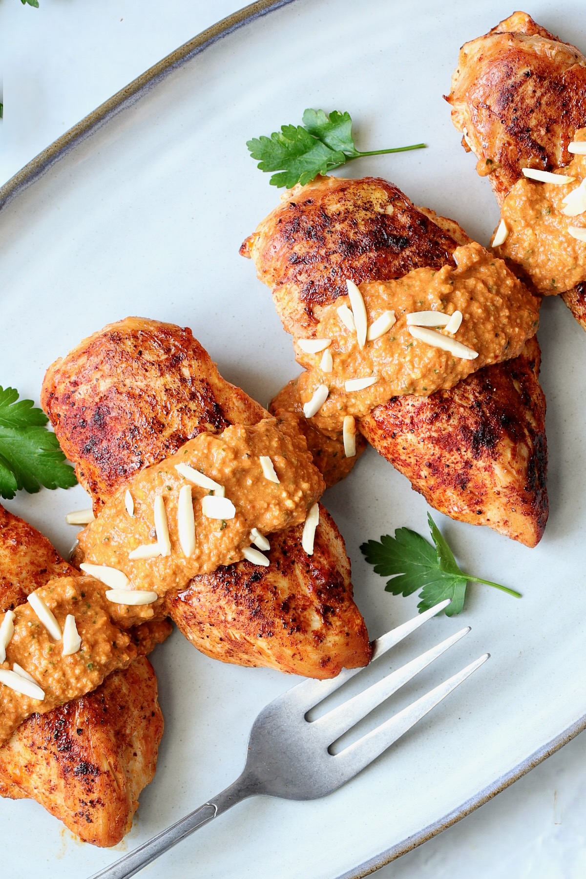 Four servings of Chicken with Romesco on gray-rimmed platter garnished with slivered almonds and parsley leaves.