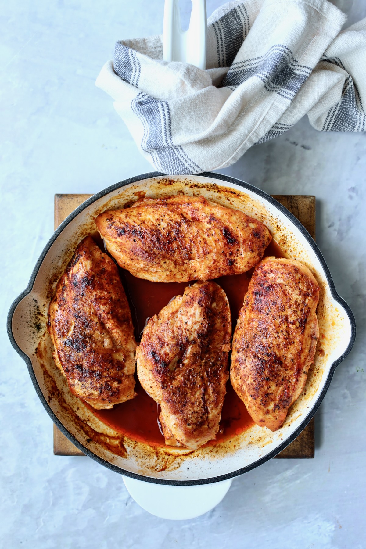 Four spice-rubbed cooked chicken breasts in white enamel cast iron skillet.