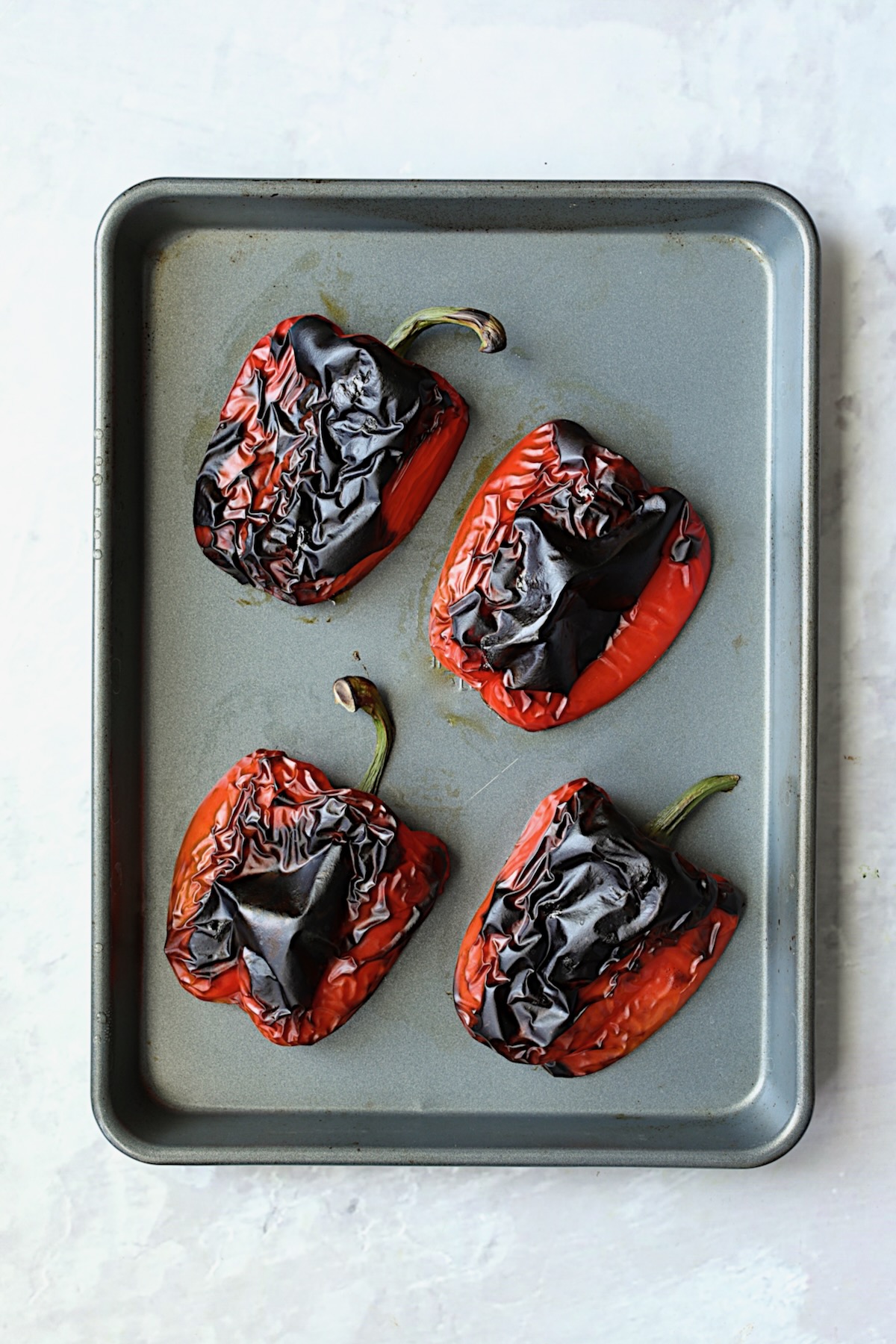 Four roasted red bell pepper halves on rimmed sheet pan.