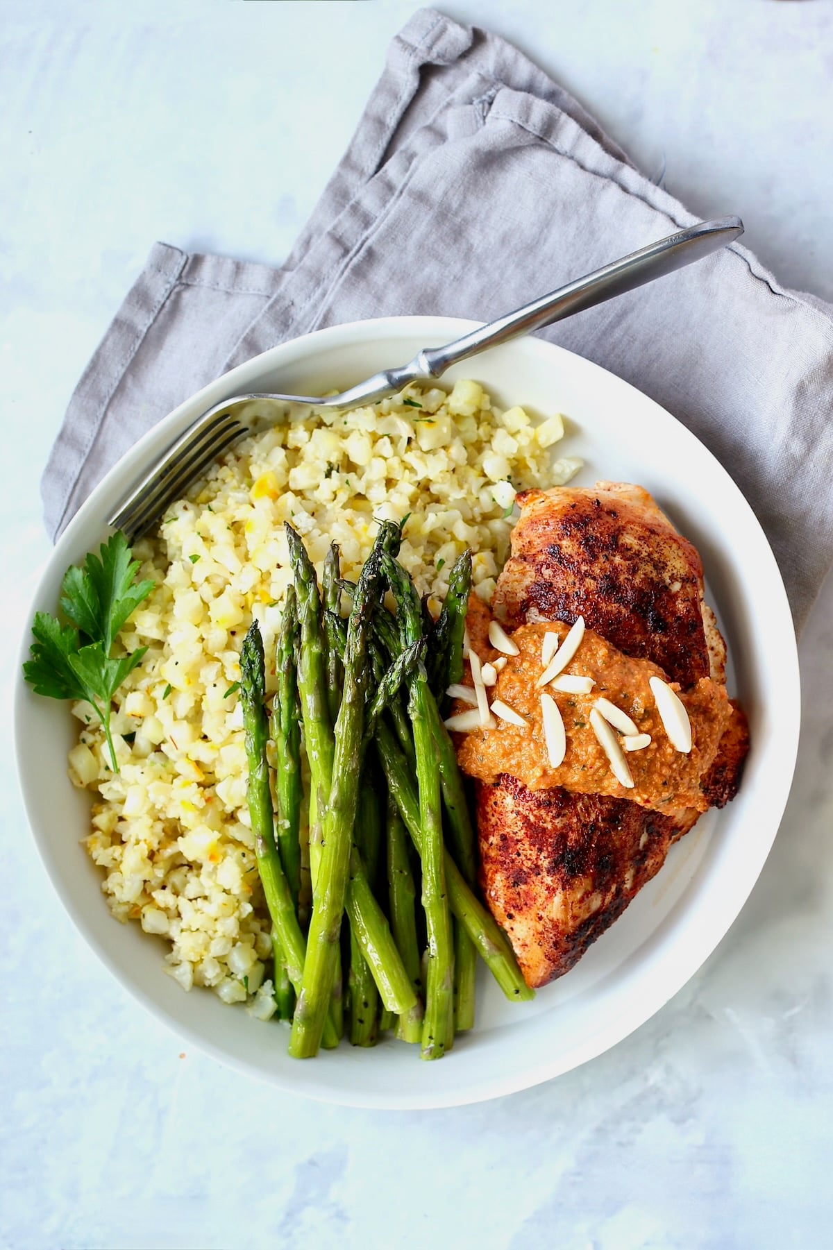 Chicken with Romesco in white dinner bowl with asparagus and cauliflower rice.