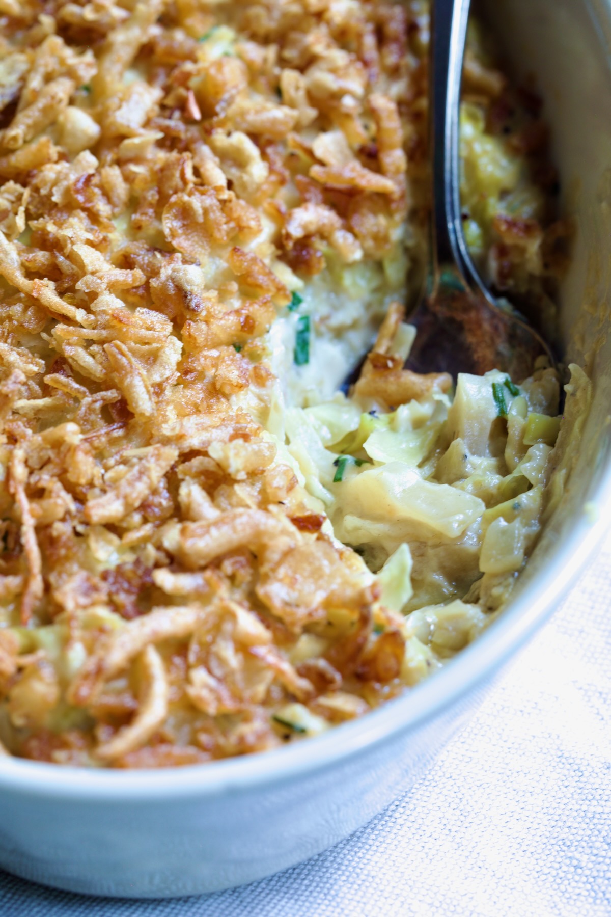Creamed Cabbage Casserole in white oval baking dish with ornate serving spoon.