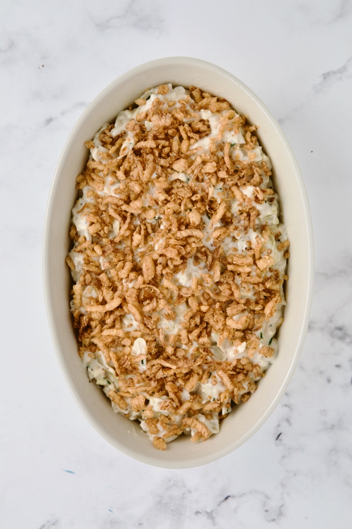Crispy onion topping added to creamed cabbage in oval white baking dish.