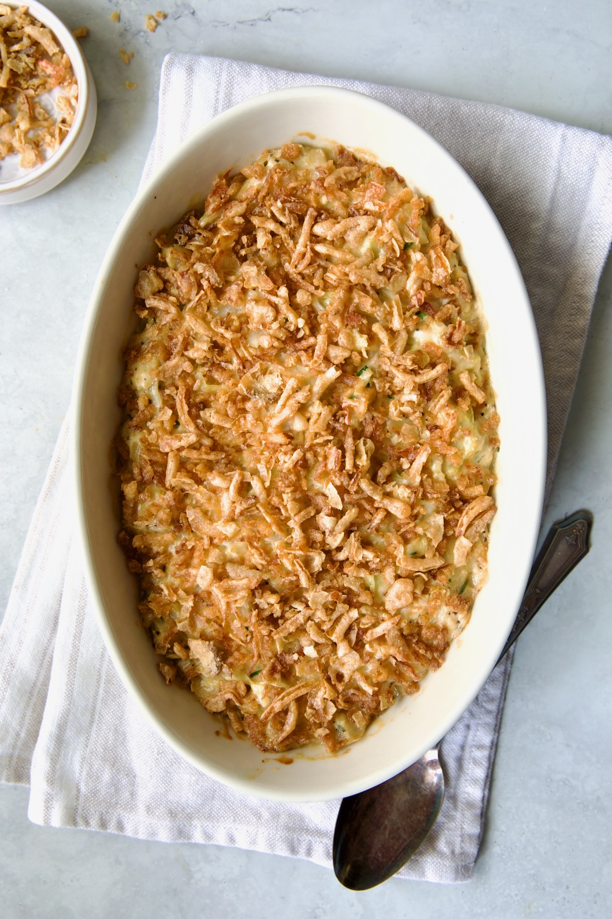 Creamed Cabbage Casserole in white oval baking dish with ornate serving spoon.
