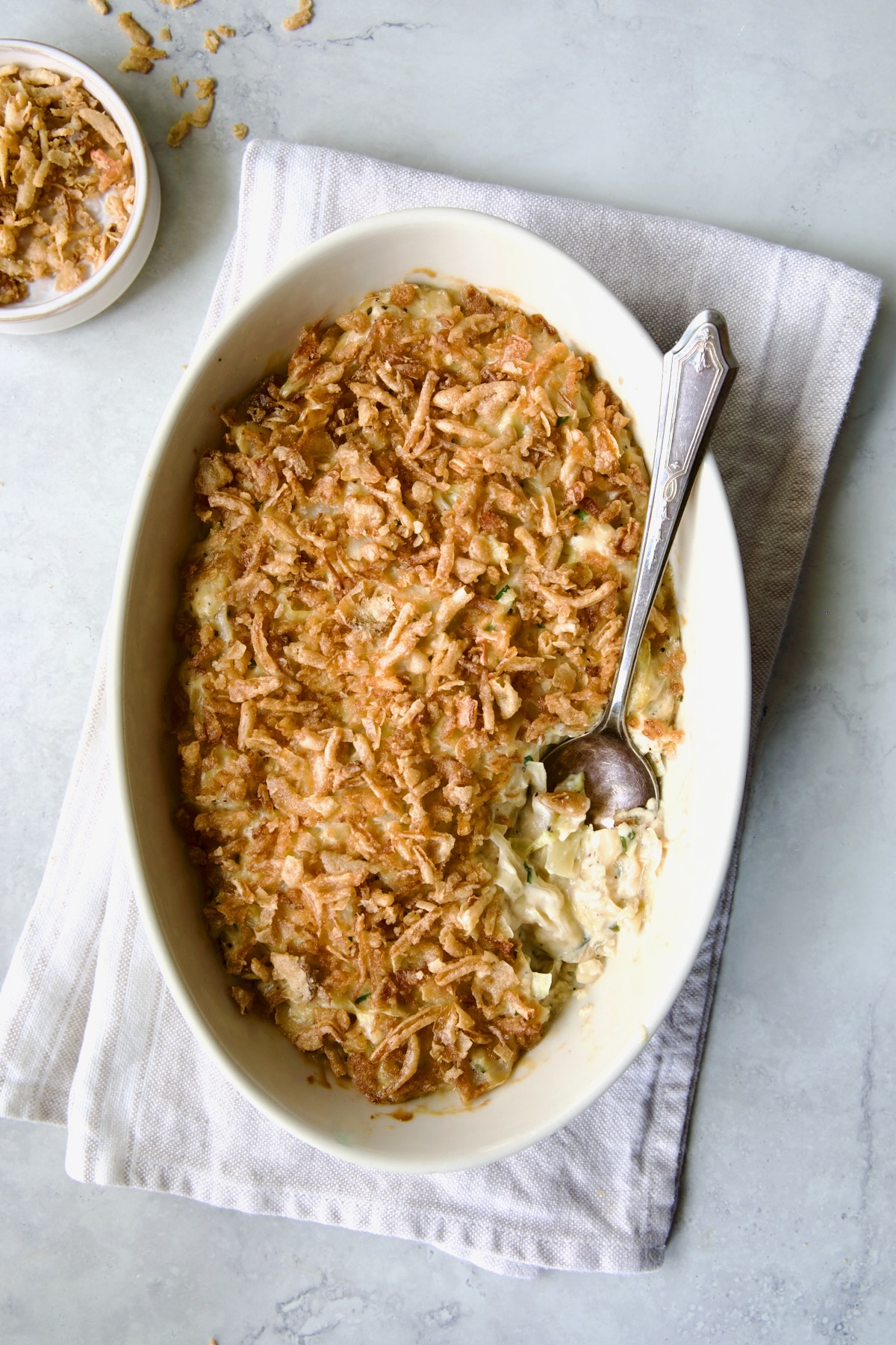 Creamed Cabbage Casserole in white oval baking dish with ornate serving spoon.