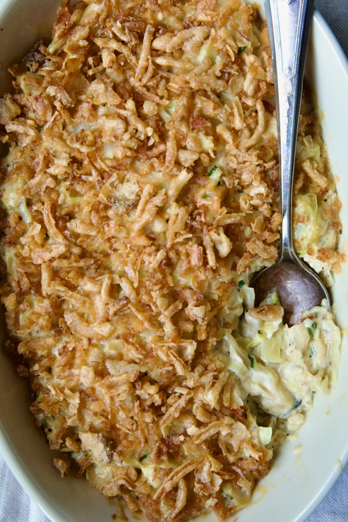 Creamed Cabbage Casserole in white oval baking dish with ornate serving spoon.