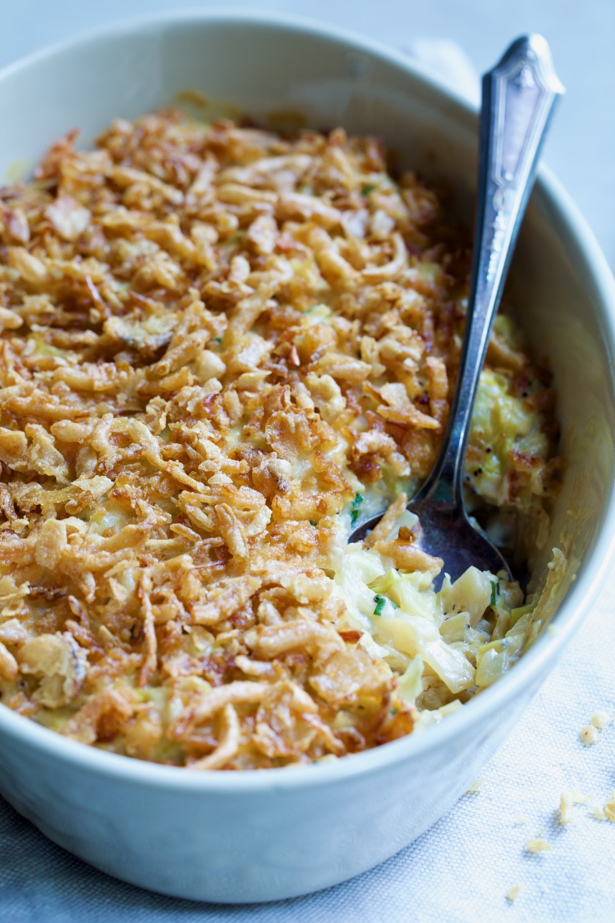 Creamed Cabbage Casserole in white oval baking dish with ornate serving spoon.