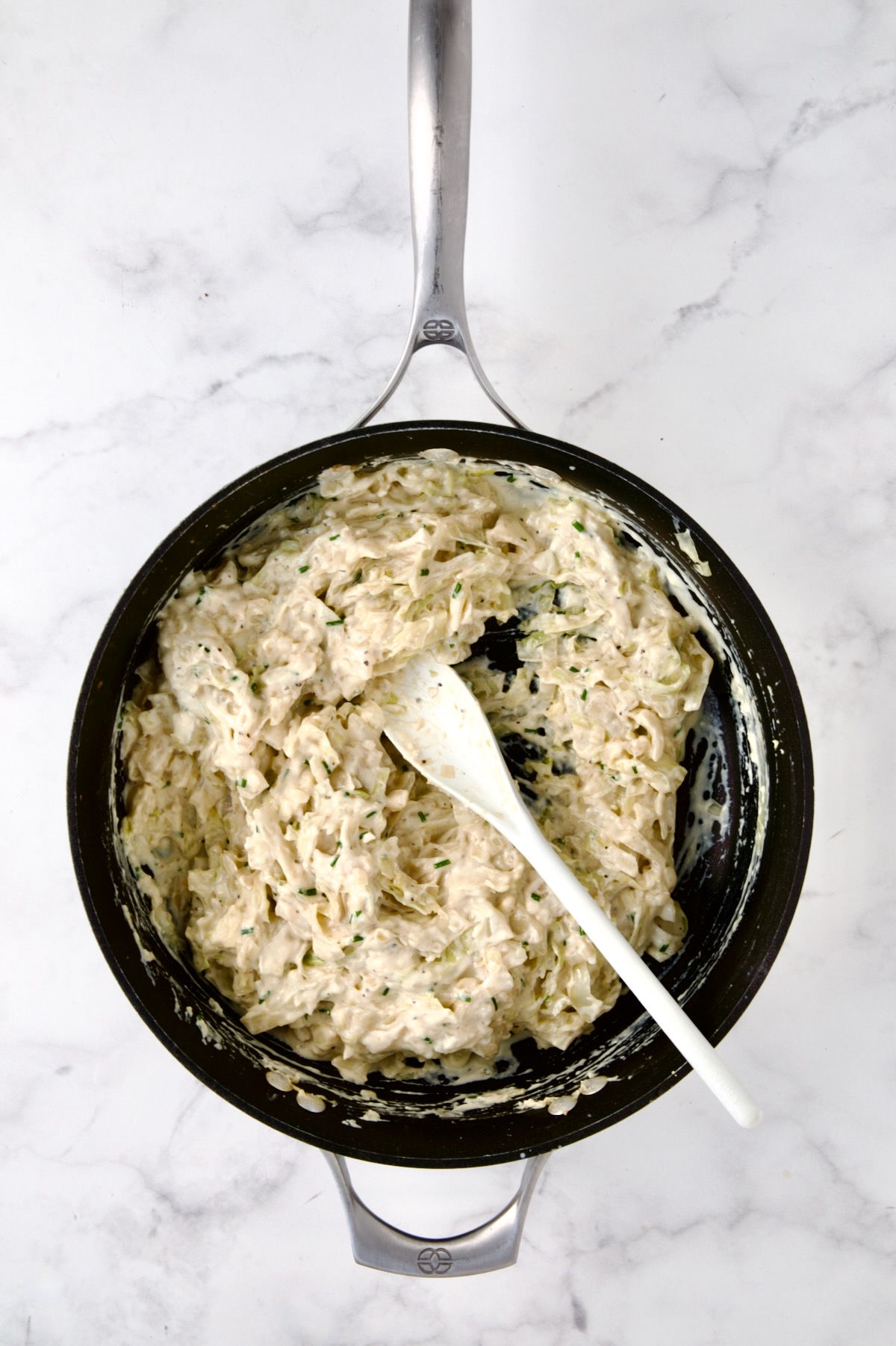Creamed cabbage in nonstick skillet being stirred with white spoon.