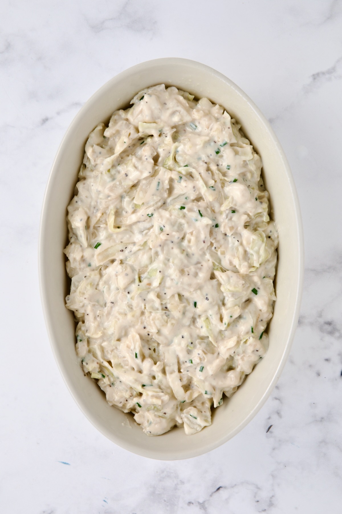 Creamed cabbage added to white oval baking dish.