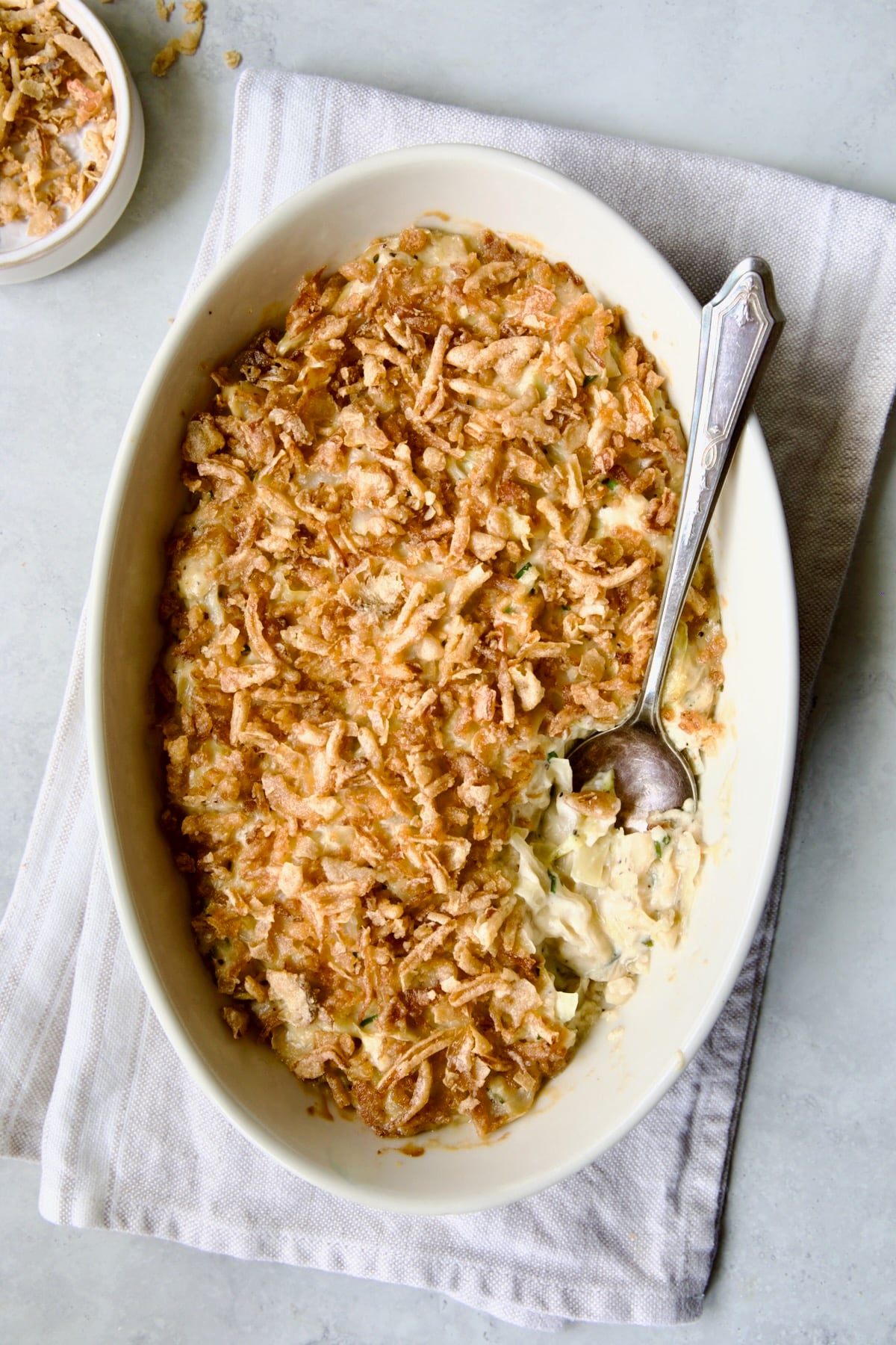 Creamed Cabbage Casserole in white oval baking dish with ornate serving spoon.