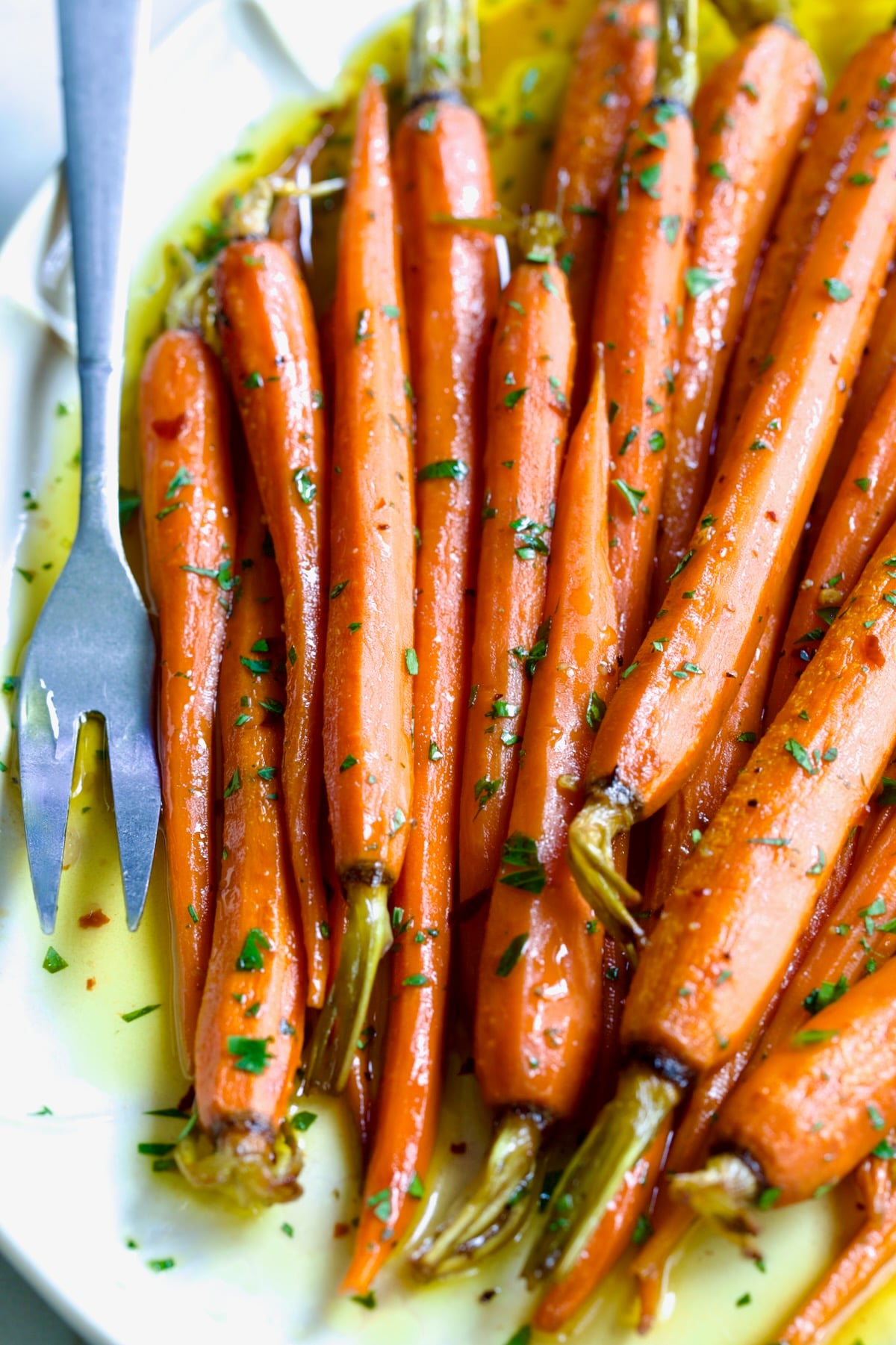 Hot Honey Roasted Carrots on white oval platter with serving fork garnished with fresh parsley.