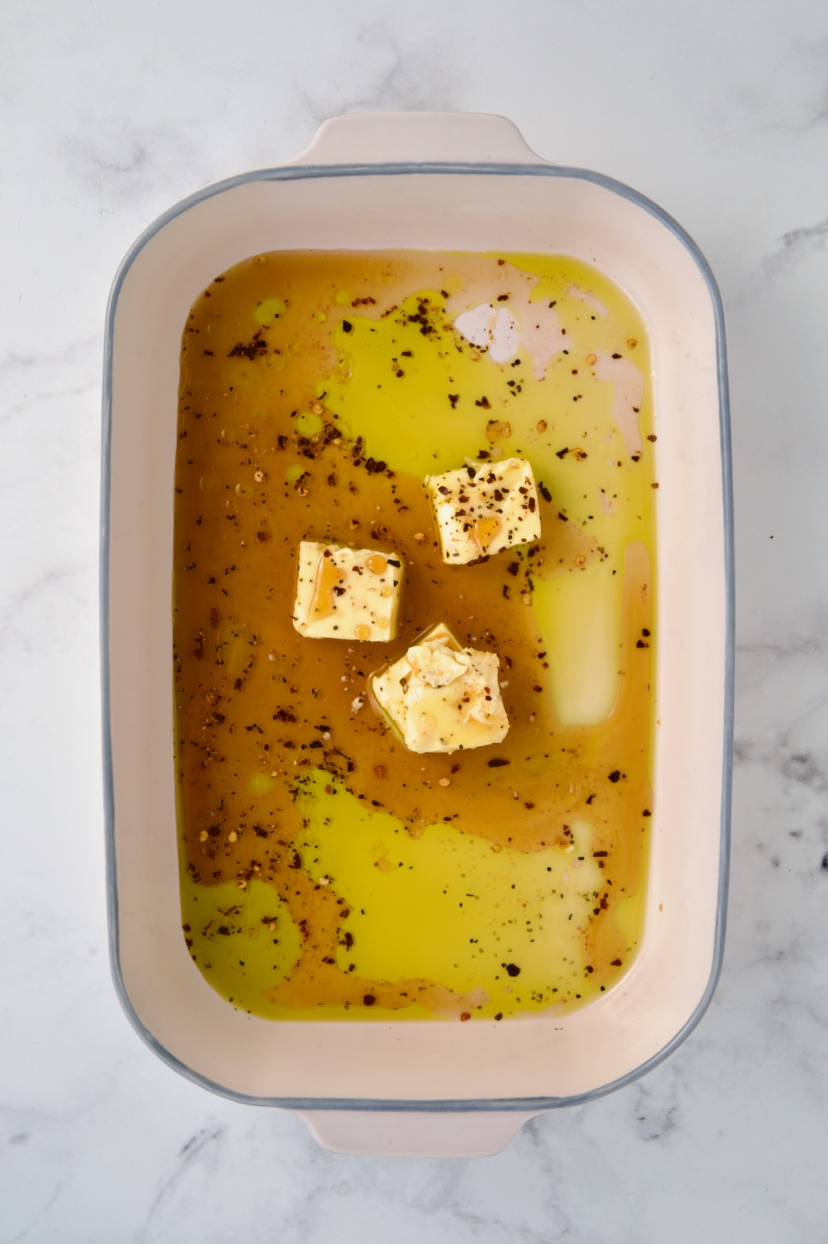 Hot honey glaze ingredients in ceramic rectangular baking dish before butter is melted.