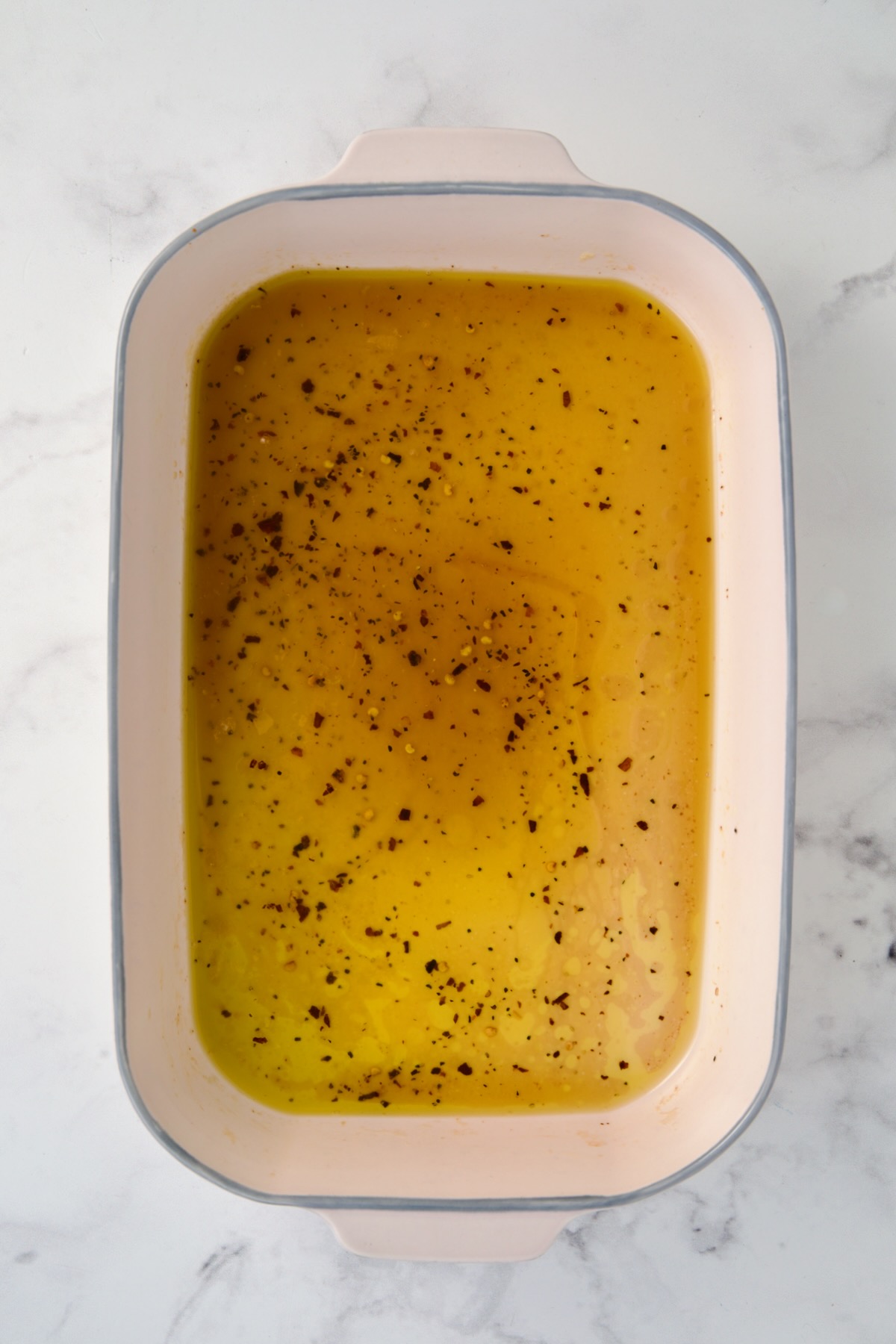 Hot honey glaze ingredients in ceramic rectangular baking dish after butter is melted.