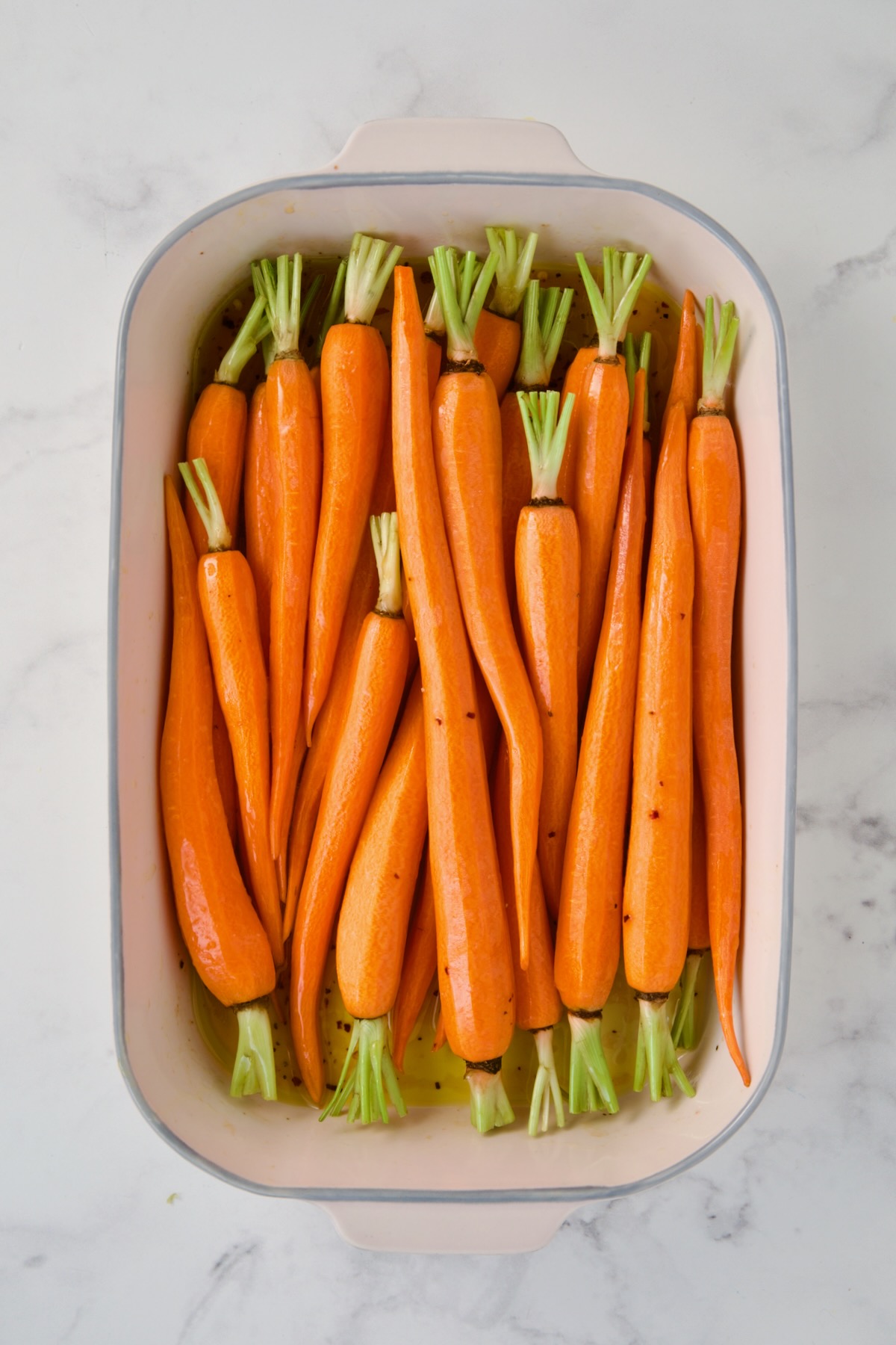 Uncooked carrots added to white rectangle baking dish.