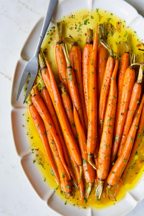 Hot Honey Roasted Carrots on white oval platter with serving fork garnished with fresh parsley.