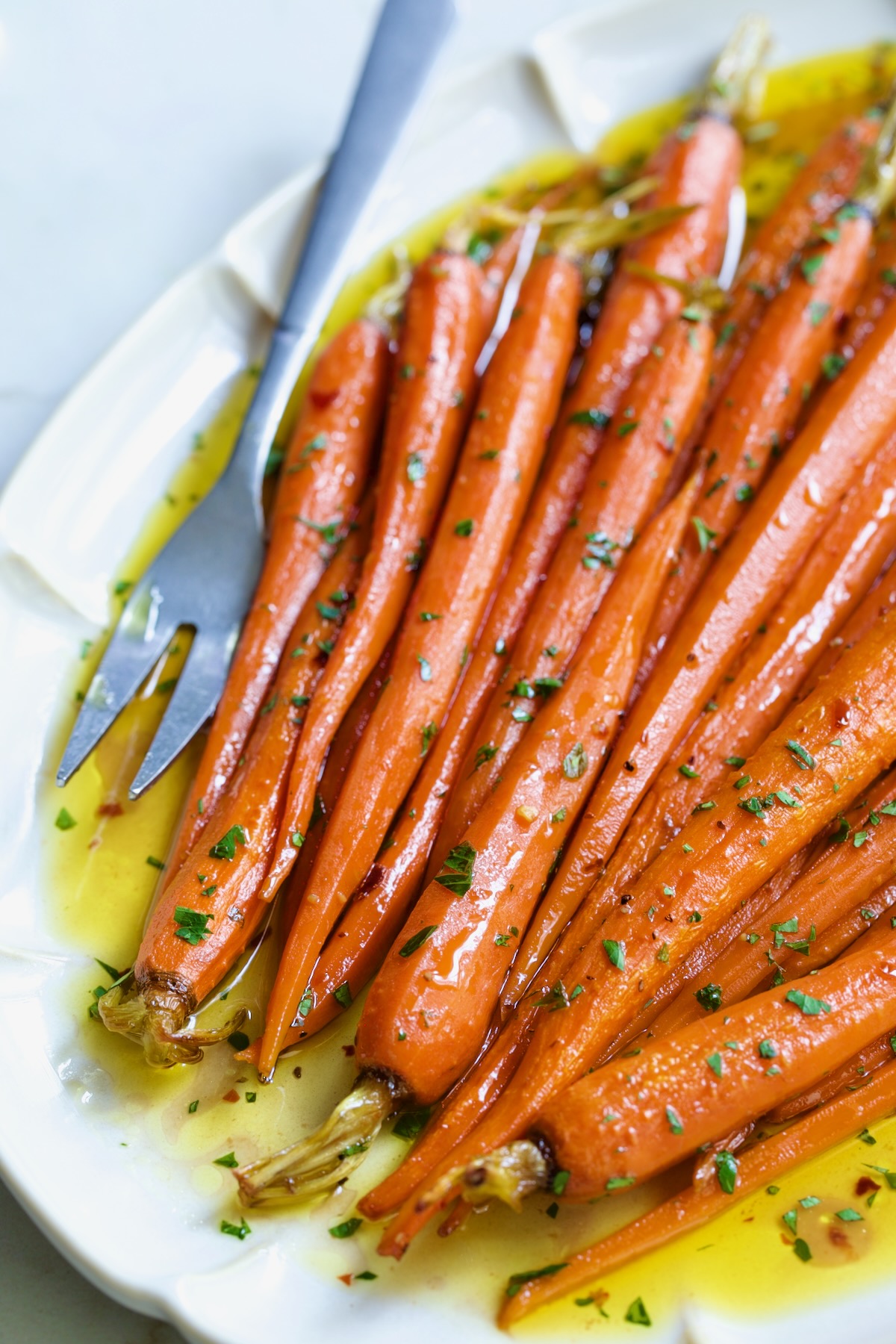 Hot Honey Roasted Carrots on white oval platter with serving fork garnished with fresh parsley.