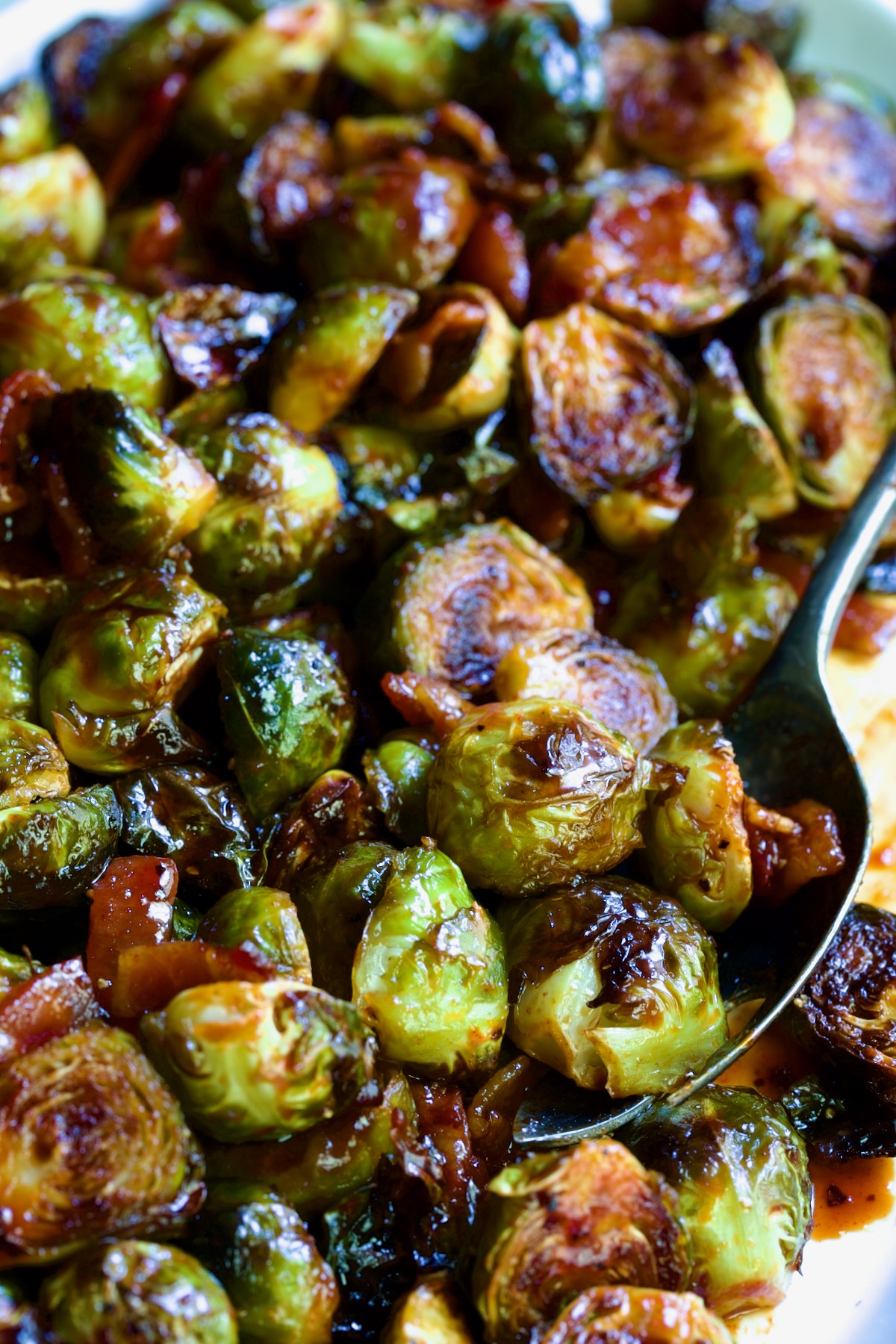 Maple Bacon Gochujang Brussels Sprouts on white platter with serving fork.