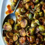 Maple Bacon Gochujang Brussels Sprouts on white platter with serving fork.
