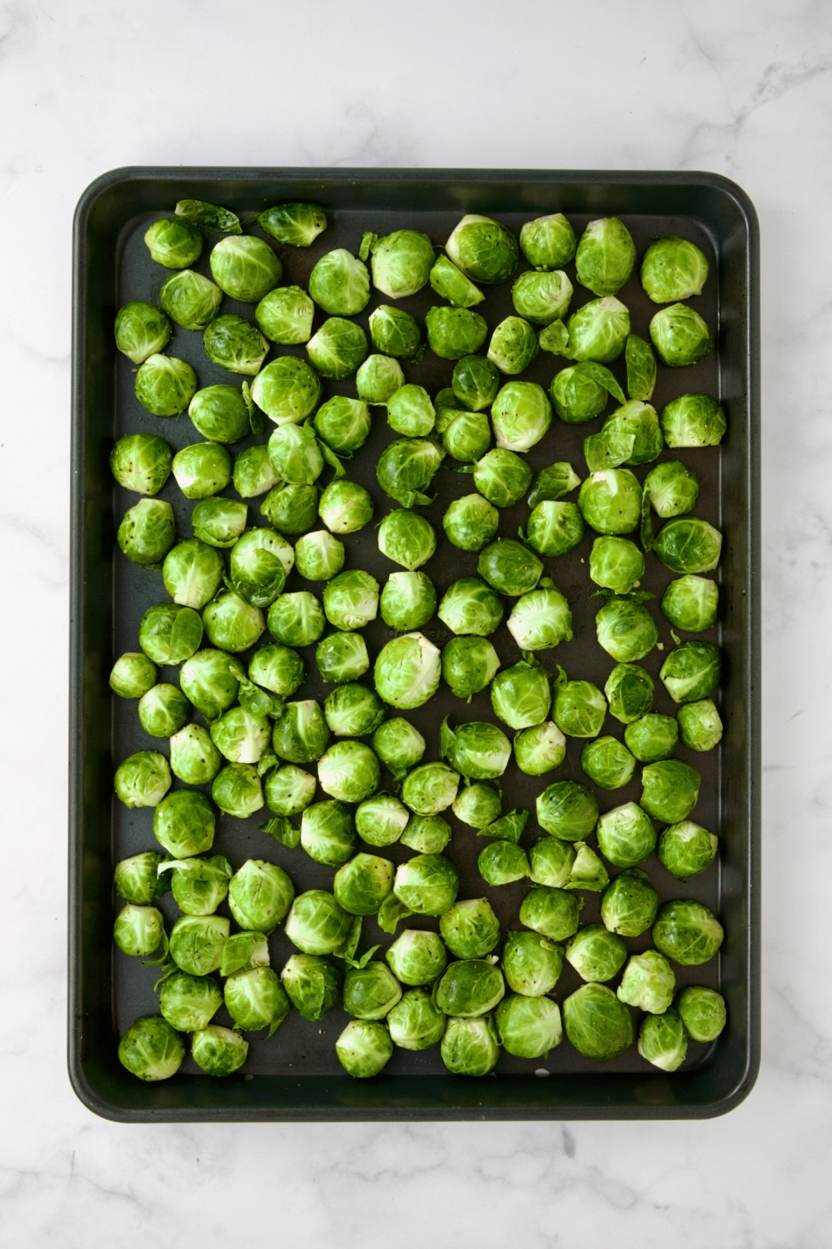 Halved Brussels sprouts on rimmed sheet pan.