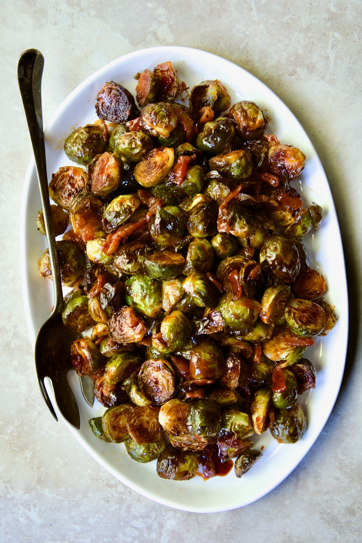 Maple Bacon Gochujang Brussels Sprouts on white platter with serving fork.