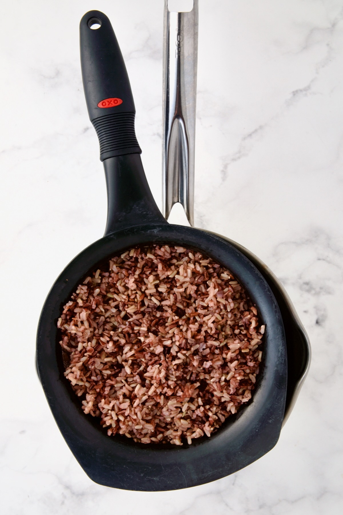 Wild rice blend being drained in black plastic colander over stainless steel saucepan.