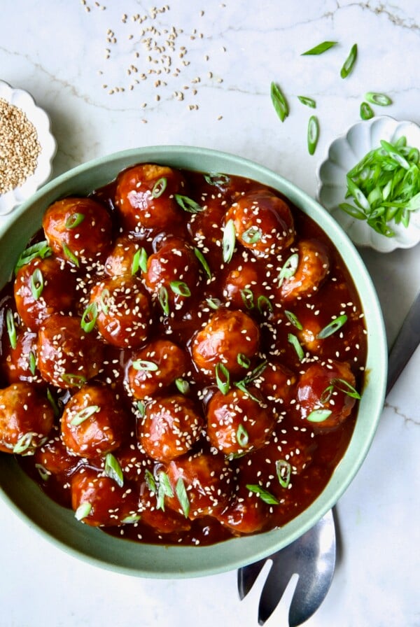 Asian Chicken Meatballs in sage green serving bowl garnished with scallions and sesame seeds.